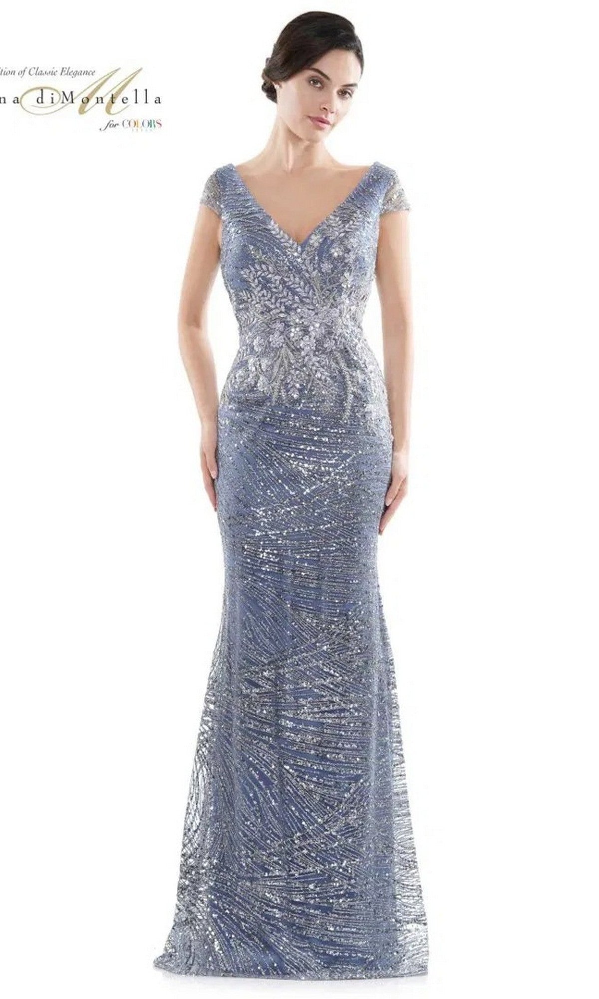 A woman wears the Rina Di Montella RD2723 long formal dress in Wedgewood, featuring a fitted, floor-length silhouette, short sleeves, a beaded bodice, and v-neckline, posed against a plain white background.